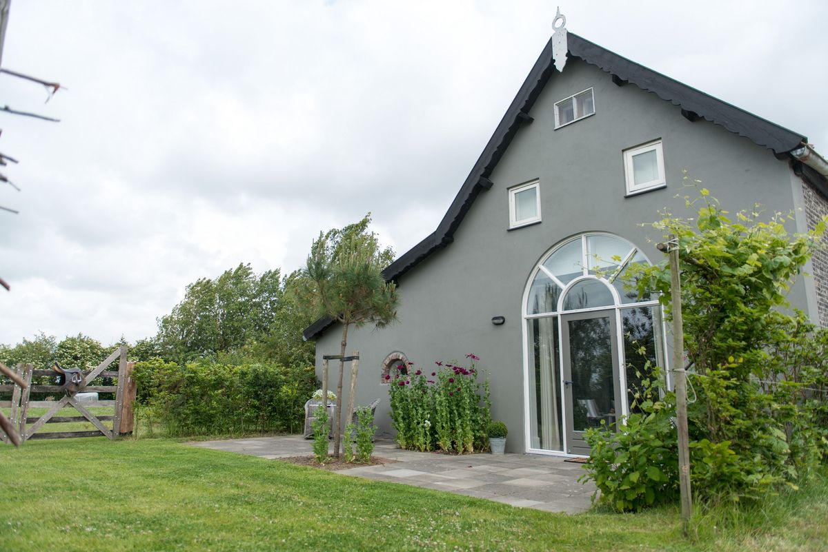 Exterieur van de verbouwde boerenstal met boogvenster en terras – Zeeuwshuisje vakantiewoning, Koudekerke