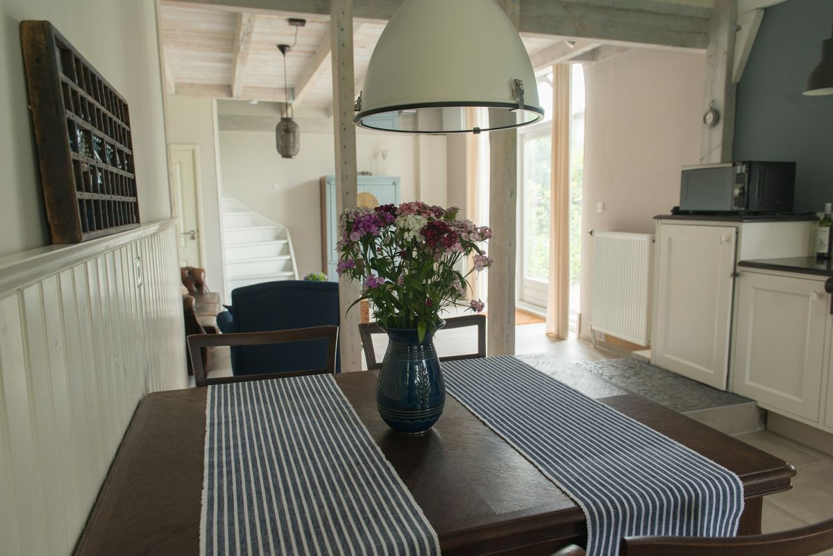 Eethoek met houten tafel en doorkijk naar de woonkamer – Zeeuwshuisje vakantiewoning, Koudekerke