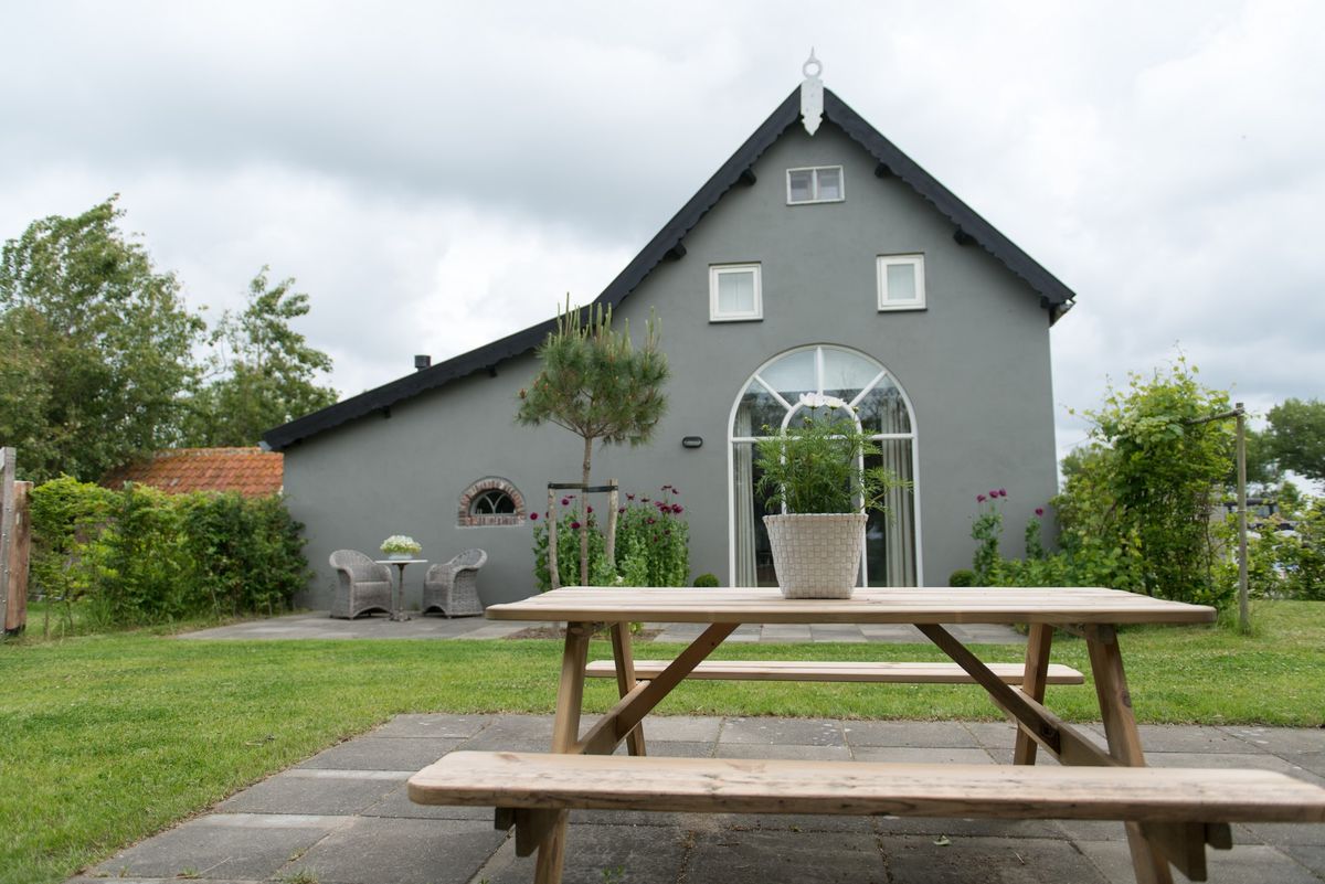 Tuinzicht met picknicktafel en gevel van de boerenstal – Zeeuwshuisje vakantiewoning, Koudekerke